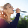 Plaatje van jonge, sportieve dame die water drinkt uit een flesje met zonneschijn op de achtergrond